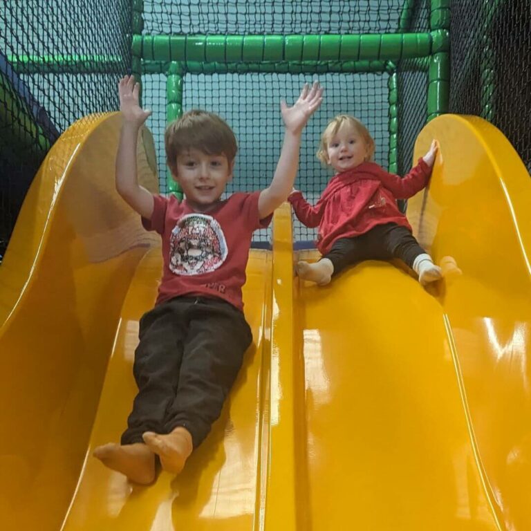 Young boy and young girl sliding down a yellow slide